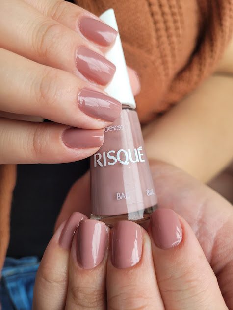 Mão com unhas em tom nude rosado segurando um esmalte