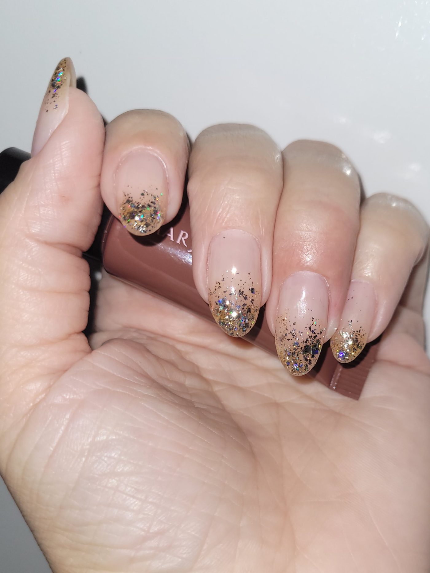 Unhas com esmaltação nude e degradê de glitter dourado